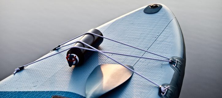 The Addison Longwood shares paddle boarding in Crystal Springs Paddle board with paddle on blue water surface background close up. Surfing and SUP boarding equipment in sunset lights close-up.