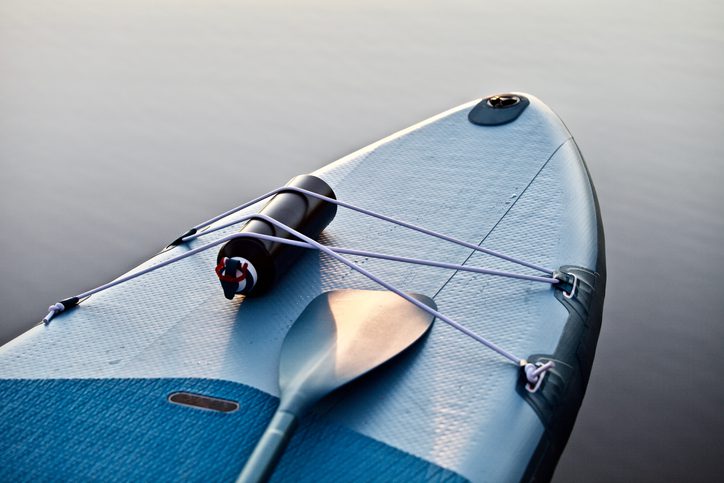 The Addison Longwood shares paddle boarding in Crystal Springs Paddle board with paddle on blue water surface background close up. Surfing and SUP boarding equipment in sunset lights close-up.
